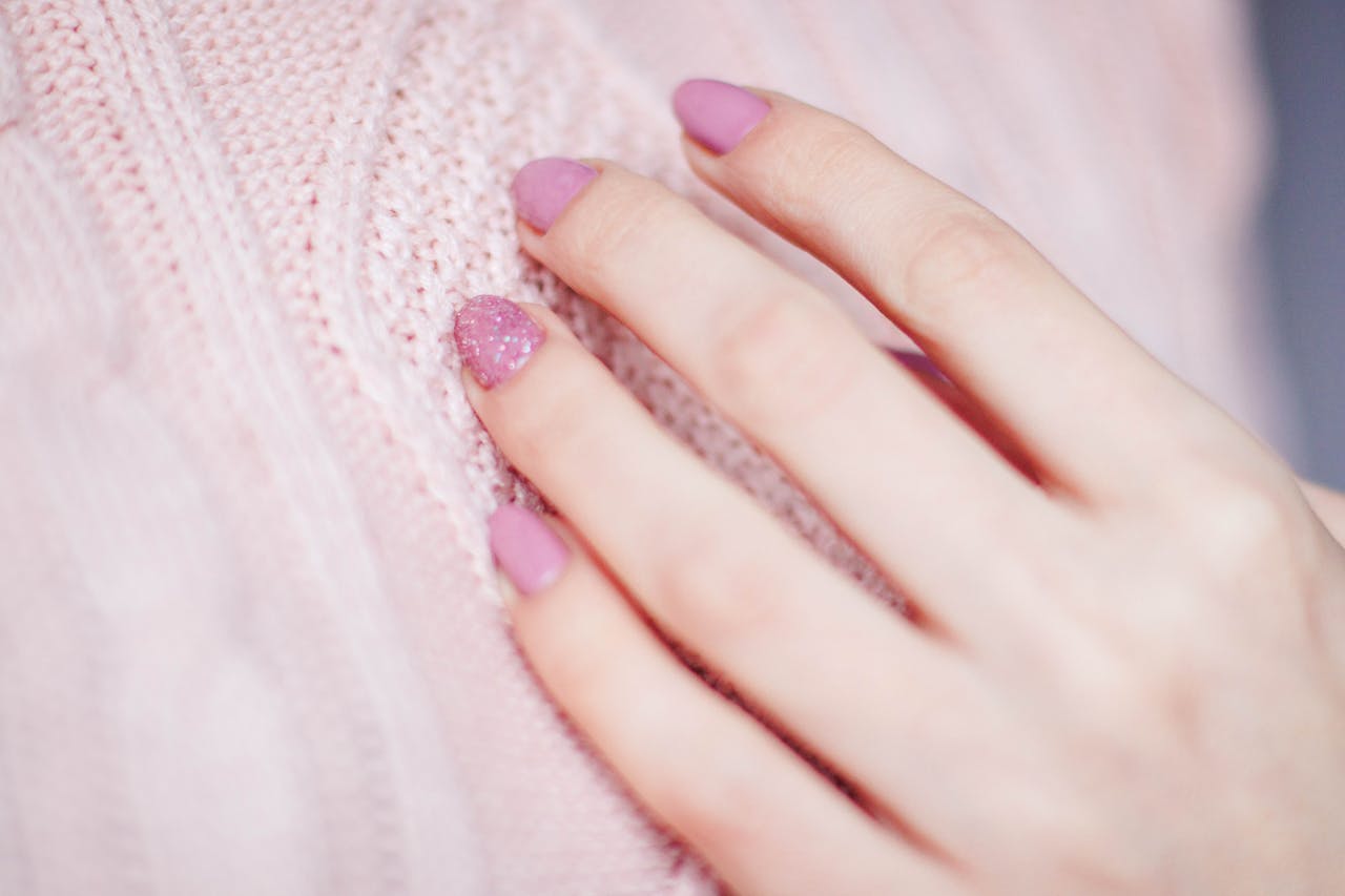 Close-up of a womans hand with pink manicure resting on a soft knit sweater, showcasing elegance and fashion.